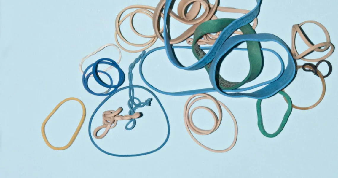 Een afbeelding van grijze en blauwe elastiekjes op een lichtblauwe achtergond, als illustratie voor dit artikel over hypermobiliteit